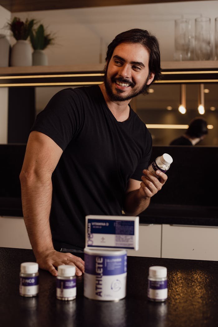 A man in a kitchen holding a supplement bottle and smiling, showcasing vitamin products.
