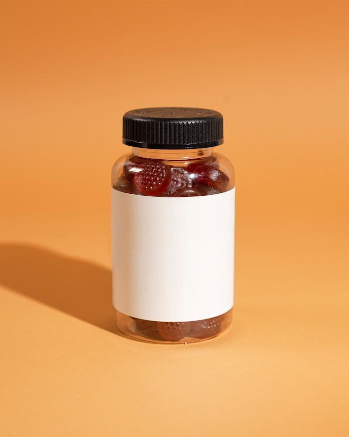 A clear bottle filled with gummy vitamins on an orange background, ideal for health and wellness themes.